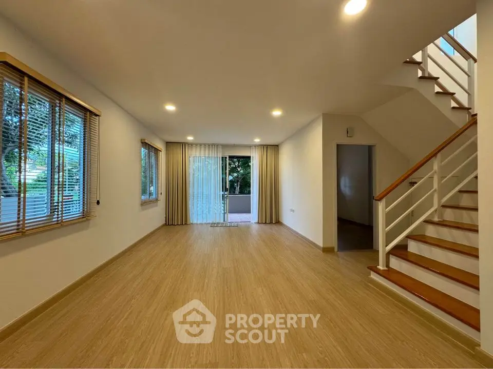 Spacious modern living room with wooden flooring and staircase, ideal for family gatherings.