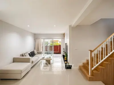 Spacious modern living room with elegant staircase and large windows opening to a balcony.