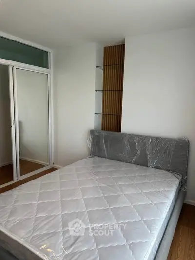 Modern bedroom with sleek design and mirrored closet doors, featuring a new mattress and stylish shelving.