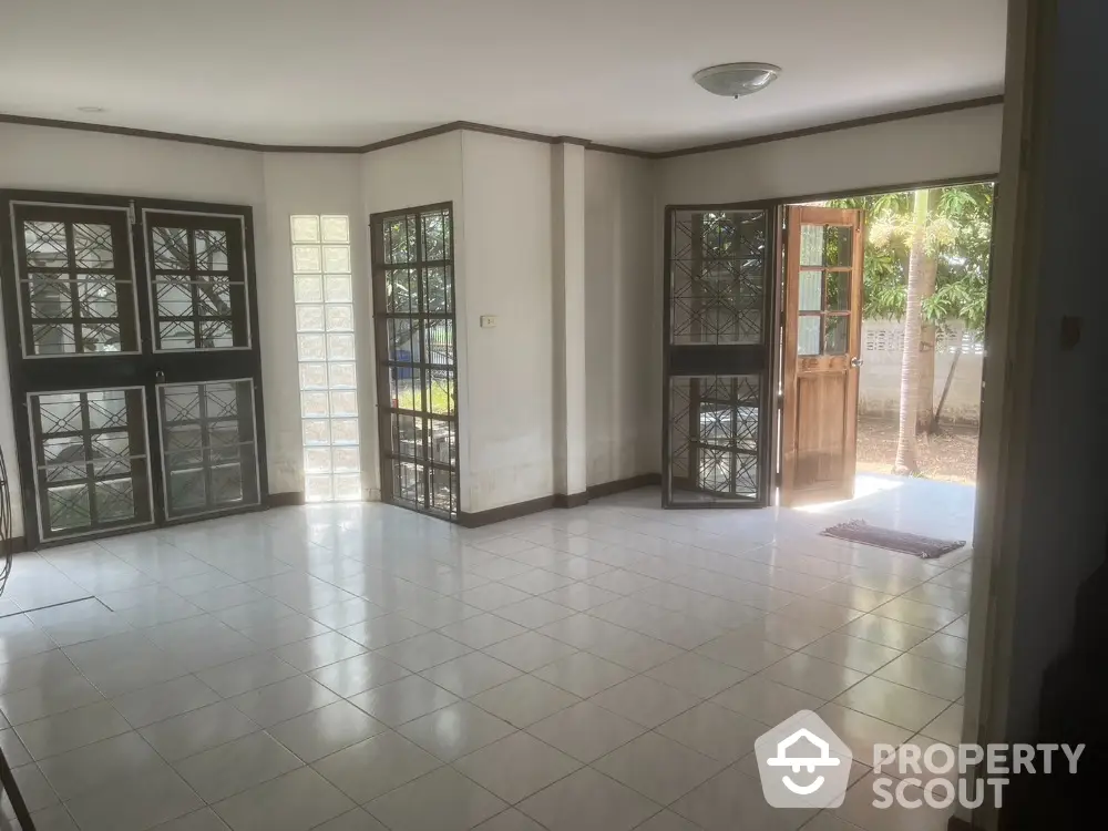 Spacious and sunlit living room with gleaming tiled floors, large windows, and glass doors leading to an inviting outdoor area, perfect for entertaining or relaxing.