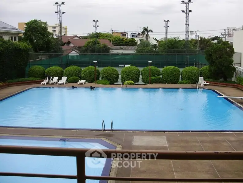 Luxurious residential pool with lush greenery and tennis courts, perfect for relaxation and recreation.