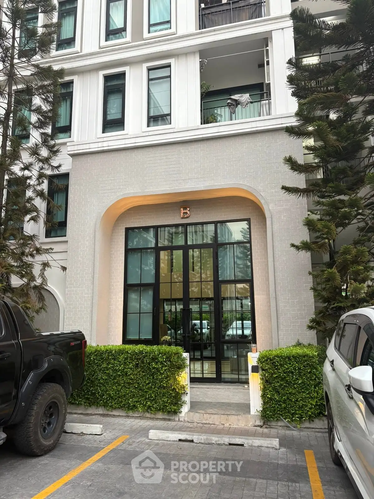Elegant apartment building entrance with modern design and lush greenery, perfect for urban living.