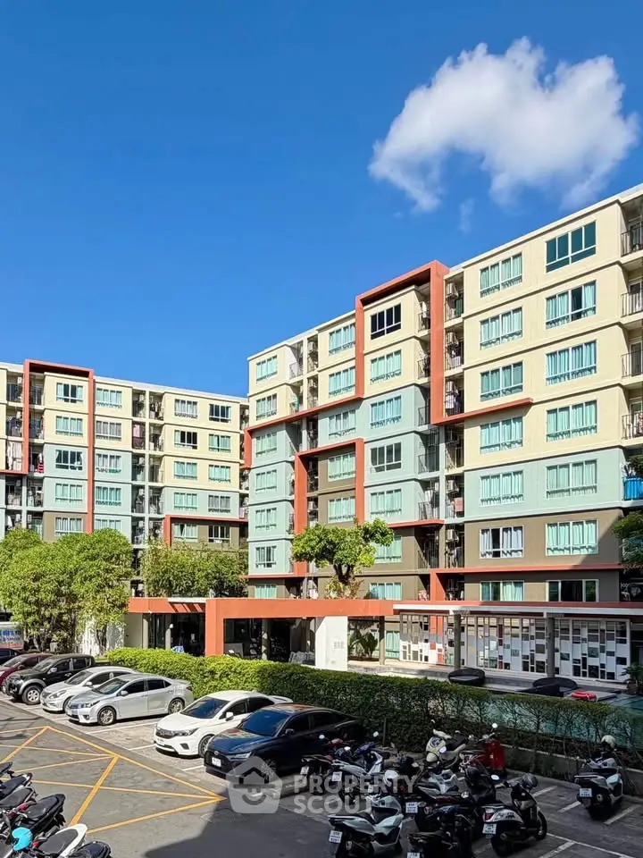 Modern apartment building with colorful facade and spacious parking area under clear blue sky.