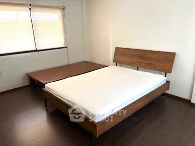 Spacious bedroom with wooden flooring and modern bed frame, ample natural light from large window.