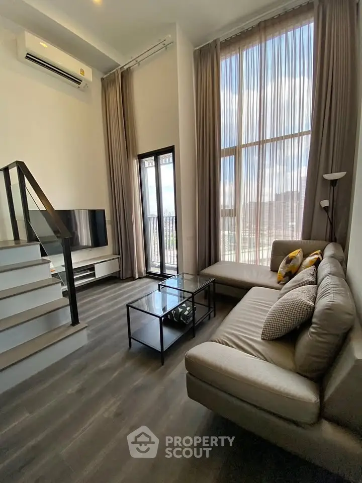 Modern living room with high ceilings and large windows, featuring a cozy sectional sofa and sleek staircase.