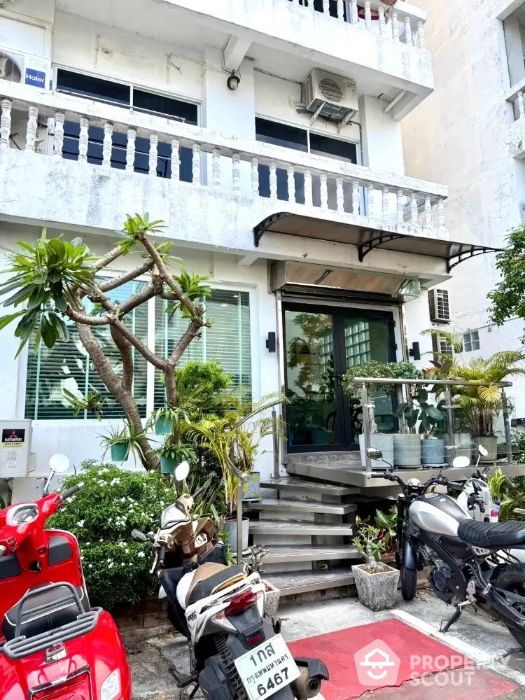 Charming urban building entrance with lush greenery and motorbike parking