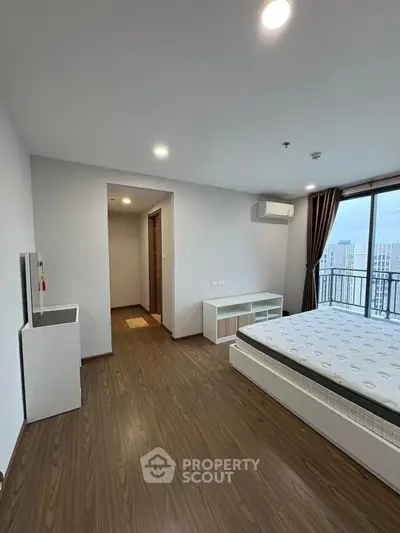 Spacious modern bedroom with balcony and wooden flooring in high-rise apartment.