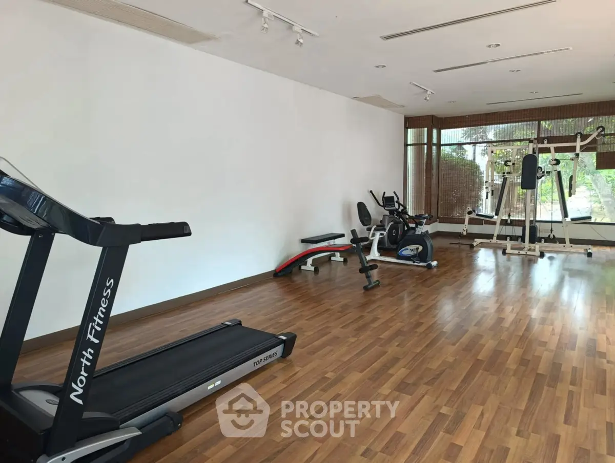 Spacious gym with modern equipment and wooden flooring in a residential complex.