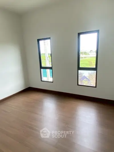 Bright empty room with wooden flooring and large windows offering natural light.