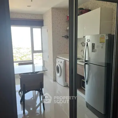 Modern kitchen with washing machine and fridge in a bright apartment with city view.