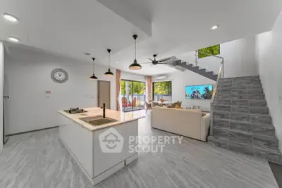 Modern open-plan living room with kitchen island and staircase, featuring large windows and stylish decor.