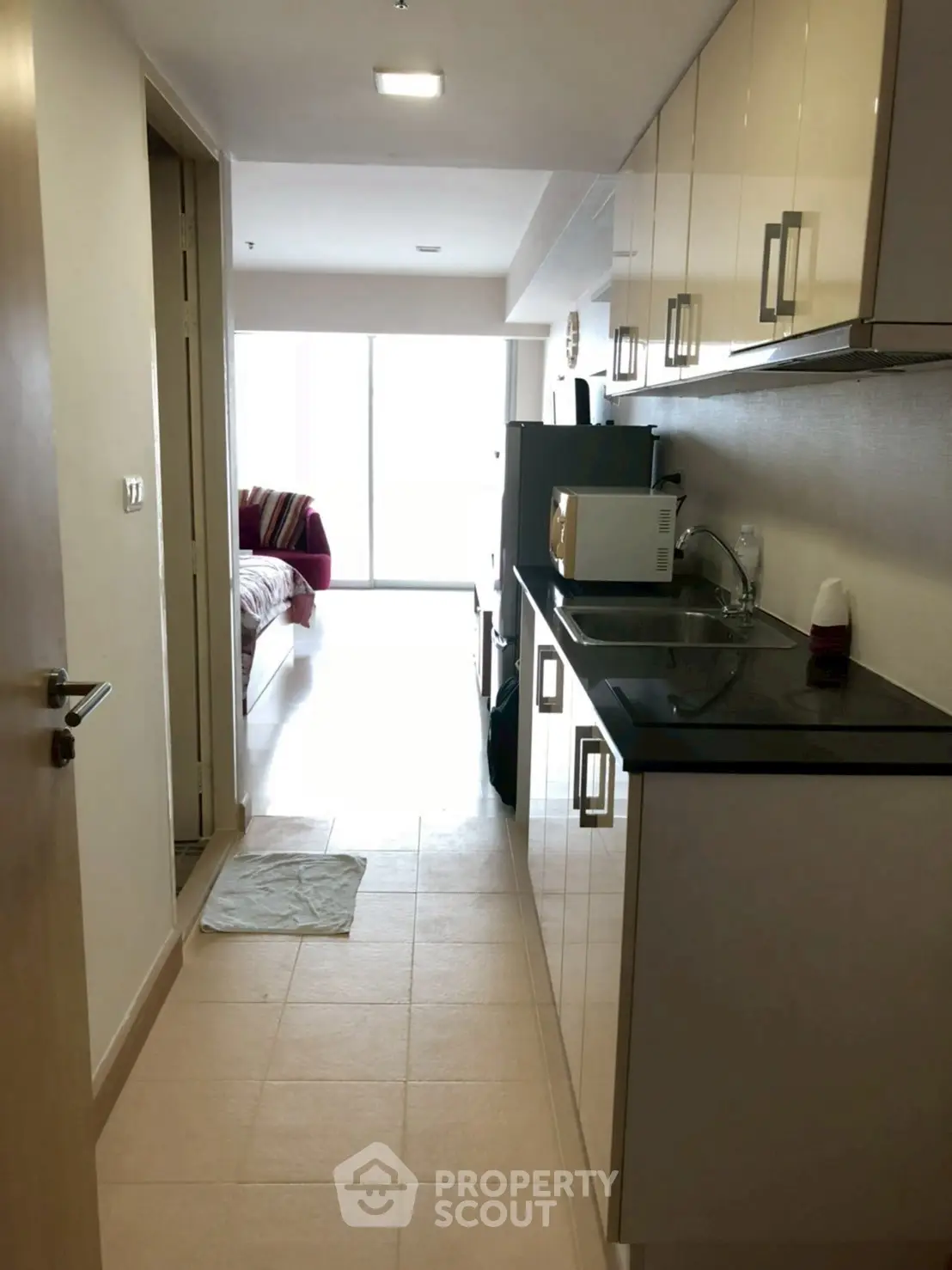Compact kitchen with modern appliances leading to a cozy bedroom in a bright apartment.