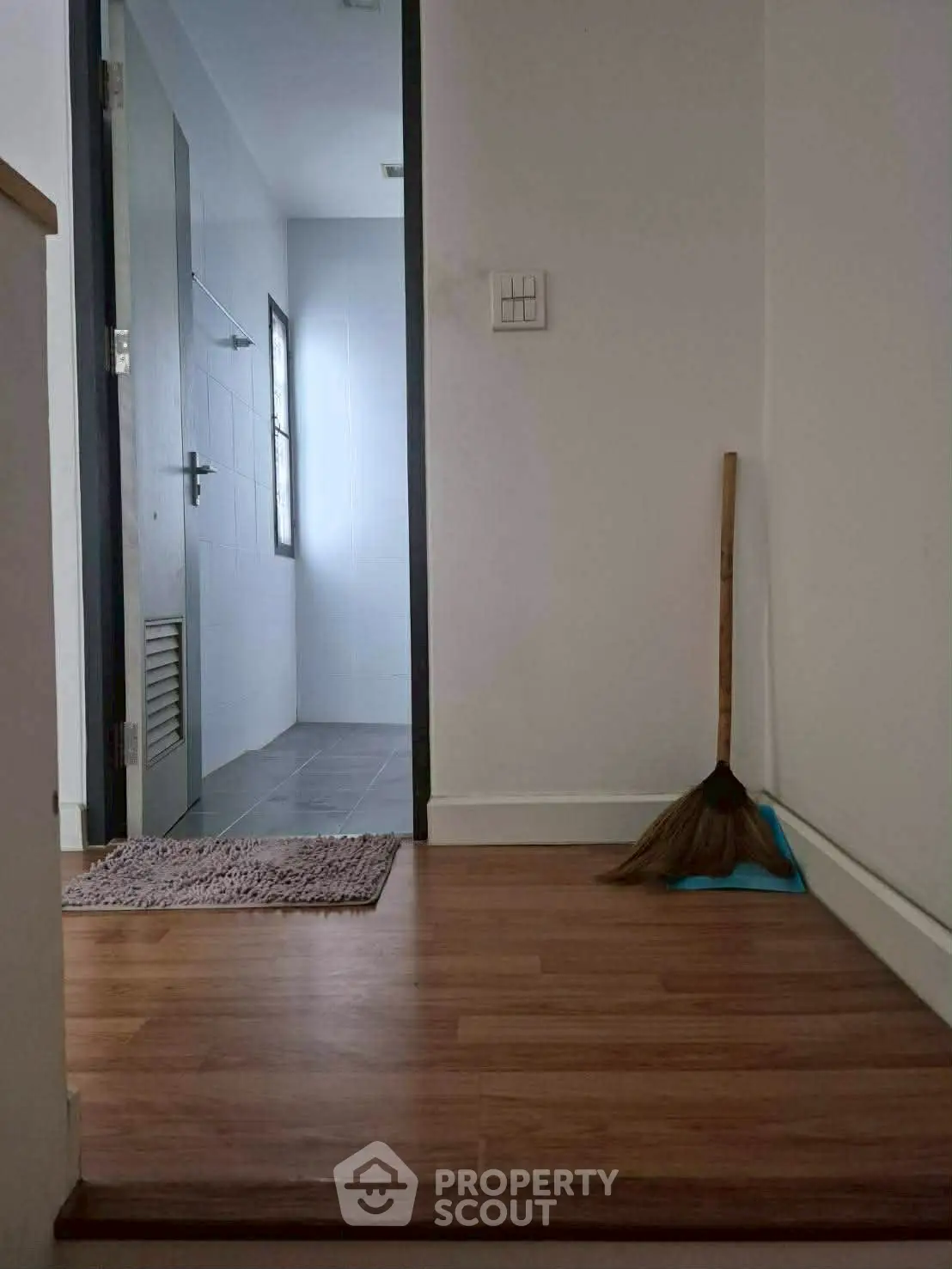 Minimalist hallway leading to a bathroom with wooden flooring and broom, perfect for cozy living.