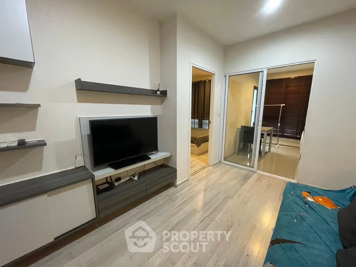 Modern living room with sleek TV setup and sliding glass doors leading to a cozy bedroom.