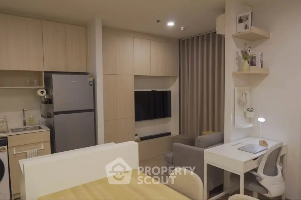 Modern open-plan living room with kitchen and study area, featuring sleek furniture and neutral tones.