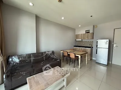 Modern open-plan living room with kitchen, featuring sleek furniture and natural lighting.
