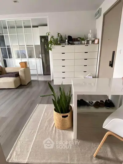 Modern living room with sleek furniture and indoor plants, featuring a stylish white dresser and glass partition.
