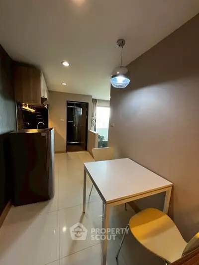 Modern kitchen with dining area in a compact apartment, featuring sleek cabinetry and contemporary lighting.