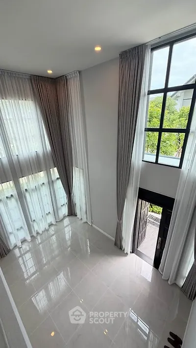 Spacious modern living room with high ceilings and large windows offering natural light and garden view.