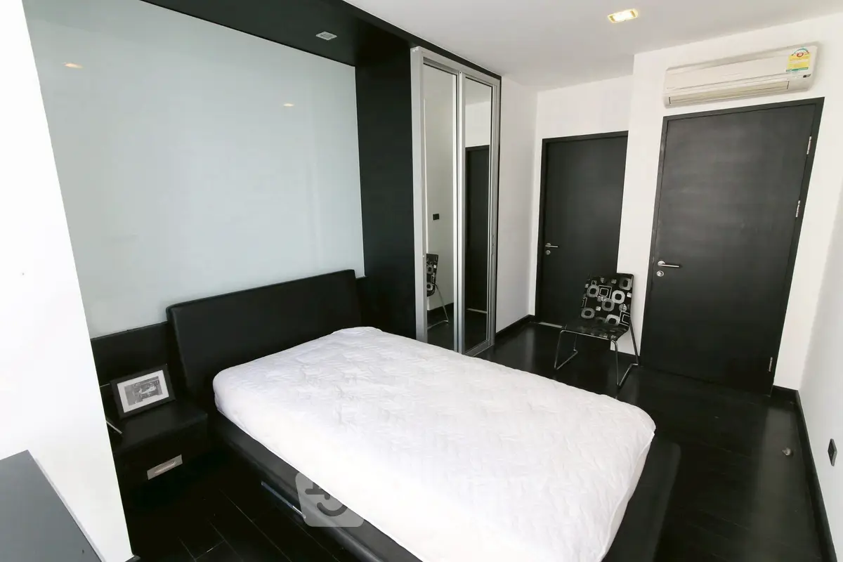 Modern minimalist bedroom with sleek black and white decor and mirrored closet doors.