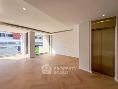 Spacious modern living room with elegant wooden flooring and large windows offering natural light.