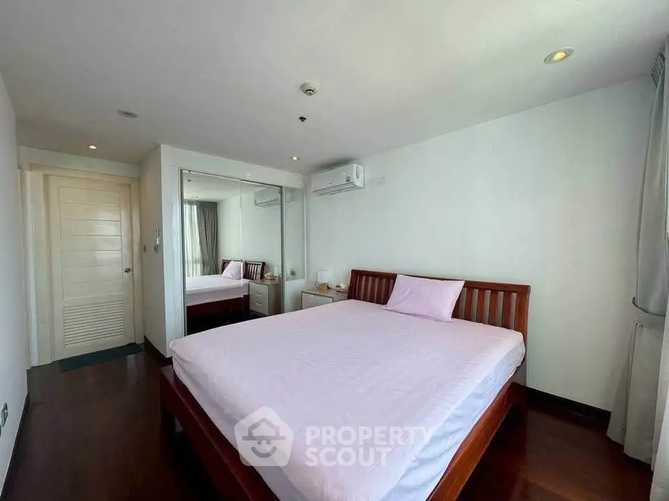 Spacious bedroom with wooden flooring and large mirror in modern apartment