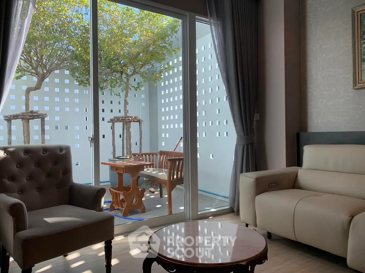 Charming living room with cozy seating and a view of a serene outdoor patio with trees.