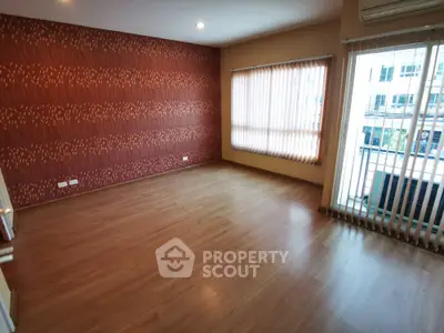 Spacious living room with elegant hardwood flooring and a unique textured accent wall, ample natural light from large window, and a cozy balcony.