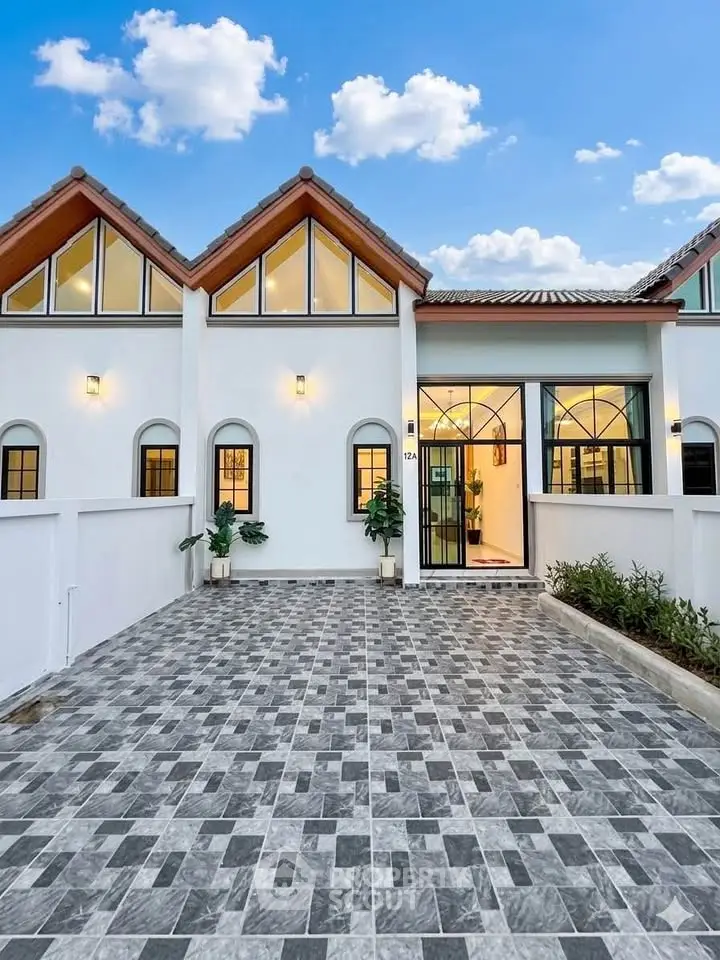 Charming modern house exterior with unique triangular roof design and spacious tiled driveway.