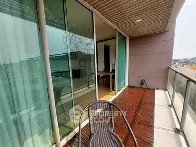 Spacious balcony with wooden flooring and glass railing offering city views.