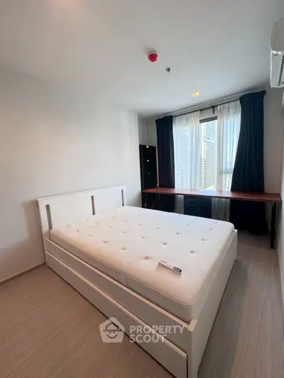 Modern bedroom with large window and city view, featuring a comfortable bed and sleek desk.