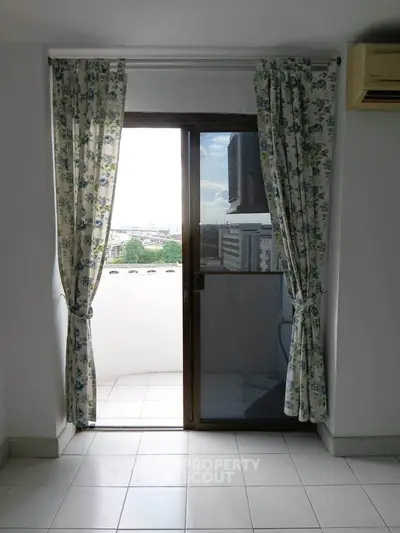 Bright room with balcony access and city view, featuring floral curtains and tiled flooring.