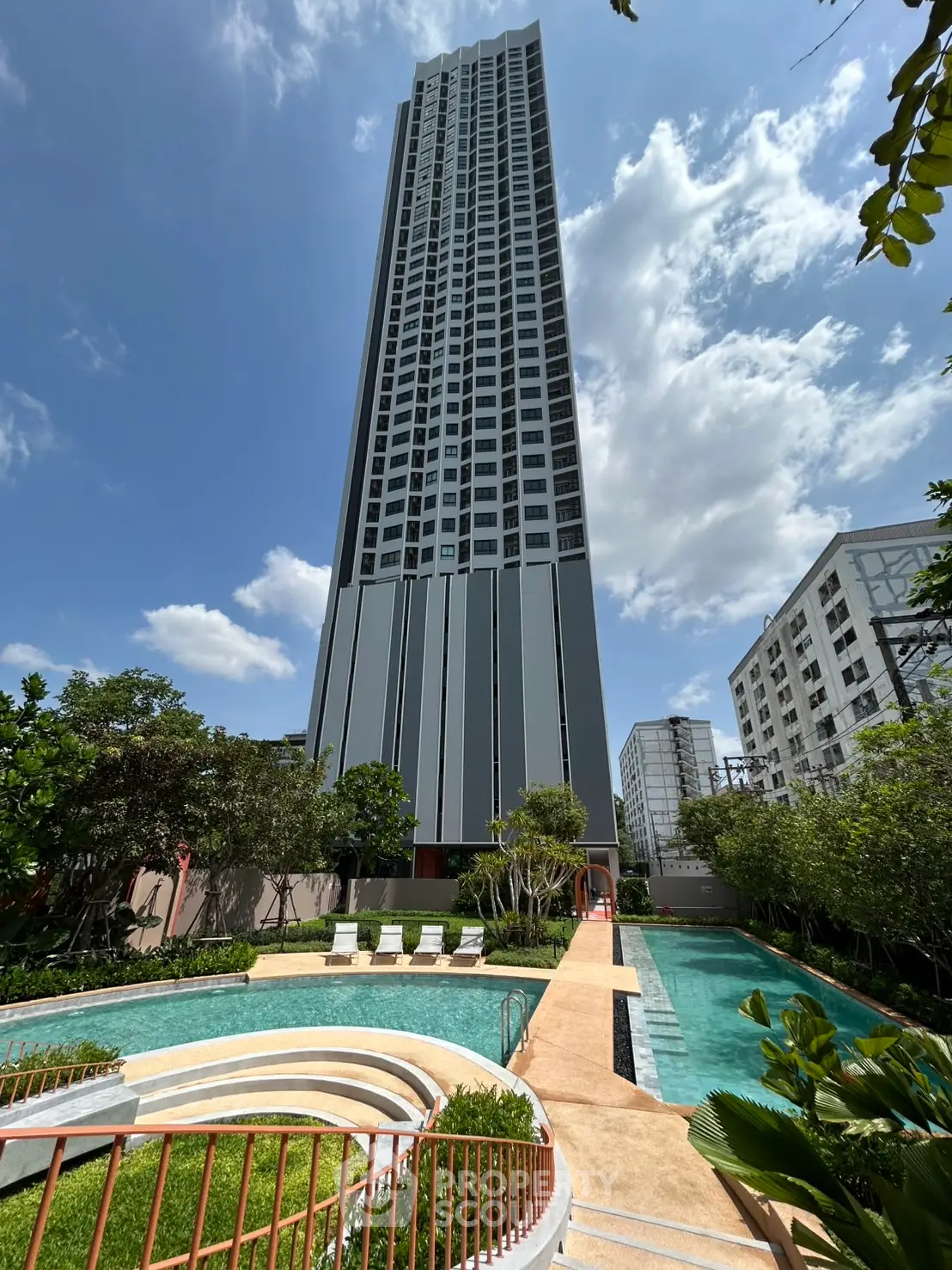 Stunning high-rise building with lush garden and inviting pool under a clear blue sky.