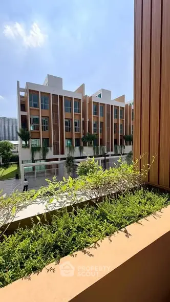 Modern townhouse exterior with lush greenery and clear blue sky, showcasing contemporary architecture.