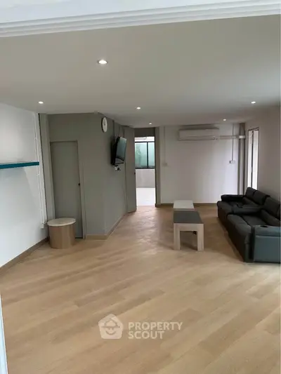 Spacious living room with modern decor and ample natural light, featuring a sleek sofa and wall-mounted TV.