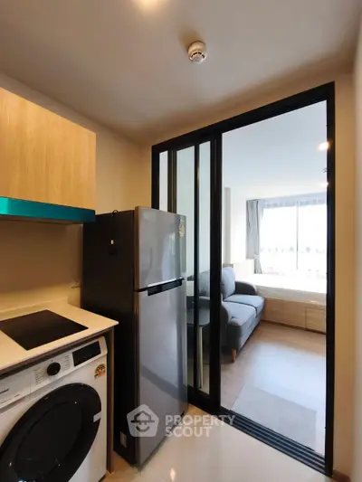Modern apartment kitchen with washing machine and fridge, open layout to living area.