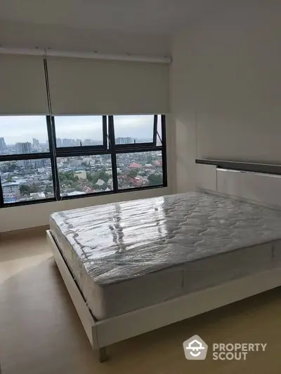 Spacious bedroom with large window offering stunning city views, featuring a modern bed frame and natural light.