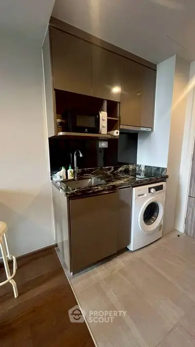 Modern compact kitchen with washing machine and microwave in sleek apartment.