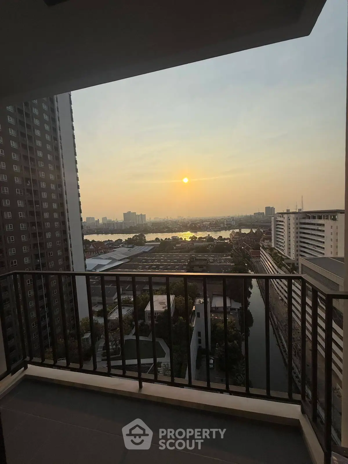 Stunning sunset view from high-rise balcony overlooking cityscape and river.