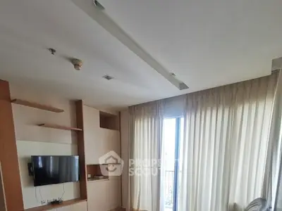 Spacious living room with modern TV setup and large window with curtains.