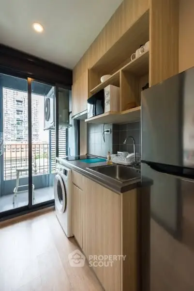 Modern compact kitchen with balcony view, featuring sleek appliances and wooden cabinetry.