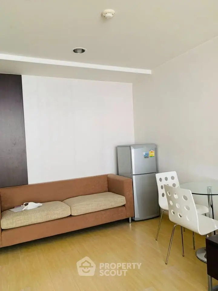 Modern living room with cozy sofa, dining set, and compact fridge in a bright apartment.