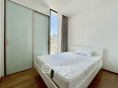 Modern bedroom with minimalist design and large window offering city view.