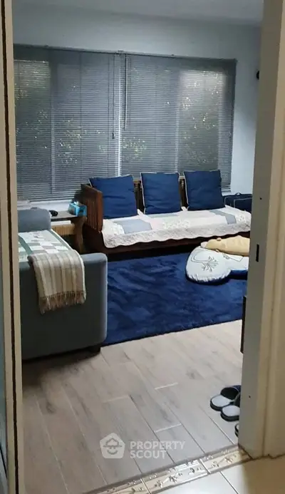 Cozy living room with wooden flooring and modern furniture, featuring a large window with blinds.