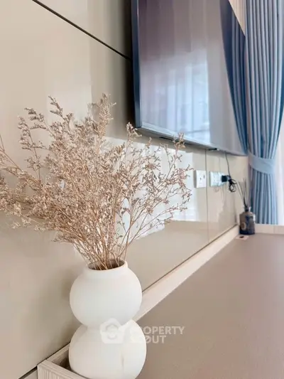 Modern living room with stylish decor and mounted TV, featuring elegant curtains and a decorative vase.