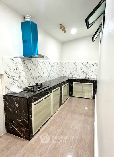 Modern kitchen with sleek marble countertops and gas stove, featuring elegant cabinetry and bright lighting.