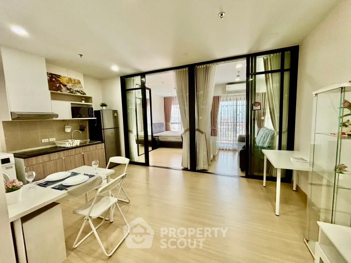 Modern open-plan living room with kitchen and glass partition to bedroom, featuring sleek design and natural light.
