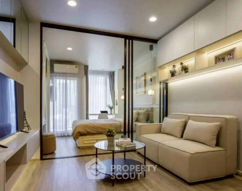 Modern living room with glass partition leading to cozy bedroom, featuring stylish decor and natural light.