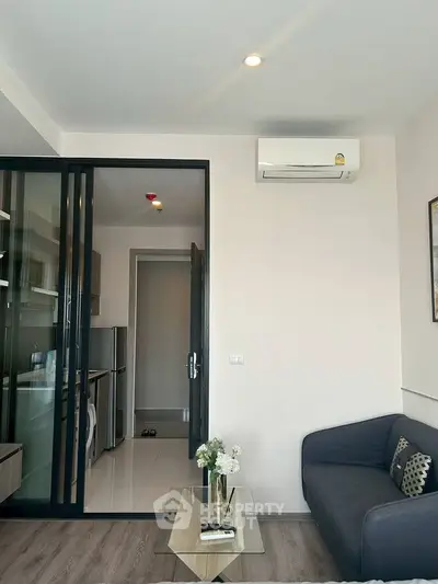 Modern living room with sleek design and air conditioning, adjacent to a compact kitchen with glass sliding doors.