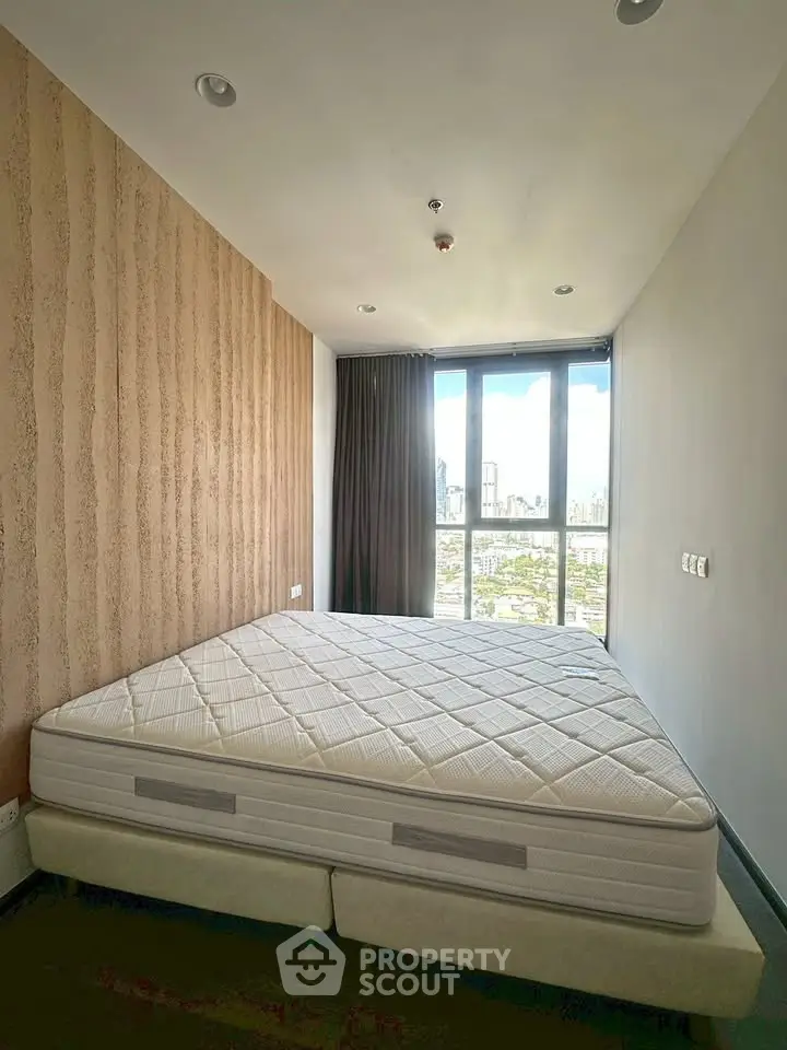 Spacious bedroom with large window offering stunning city views, featuring a comfortable bed and modern decor.